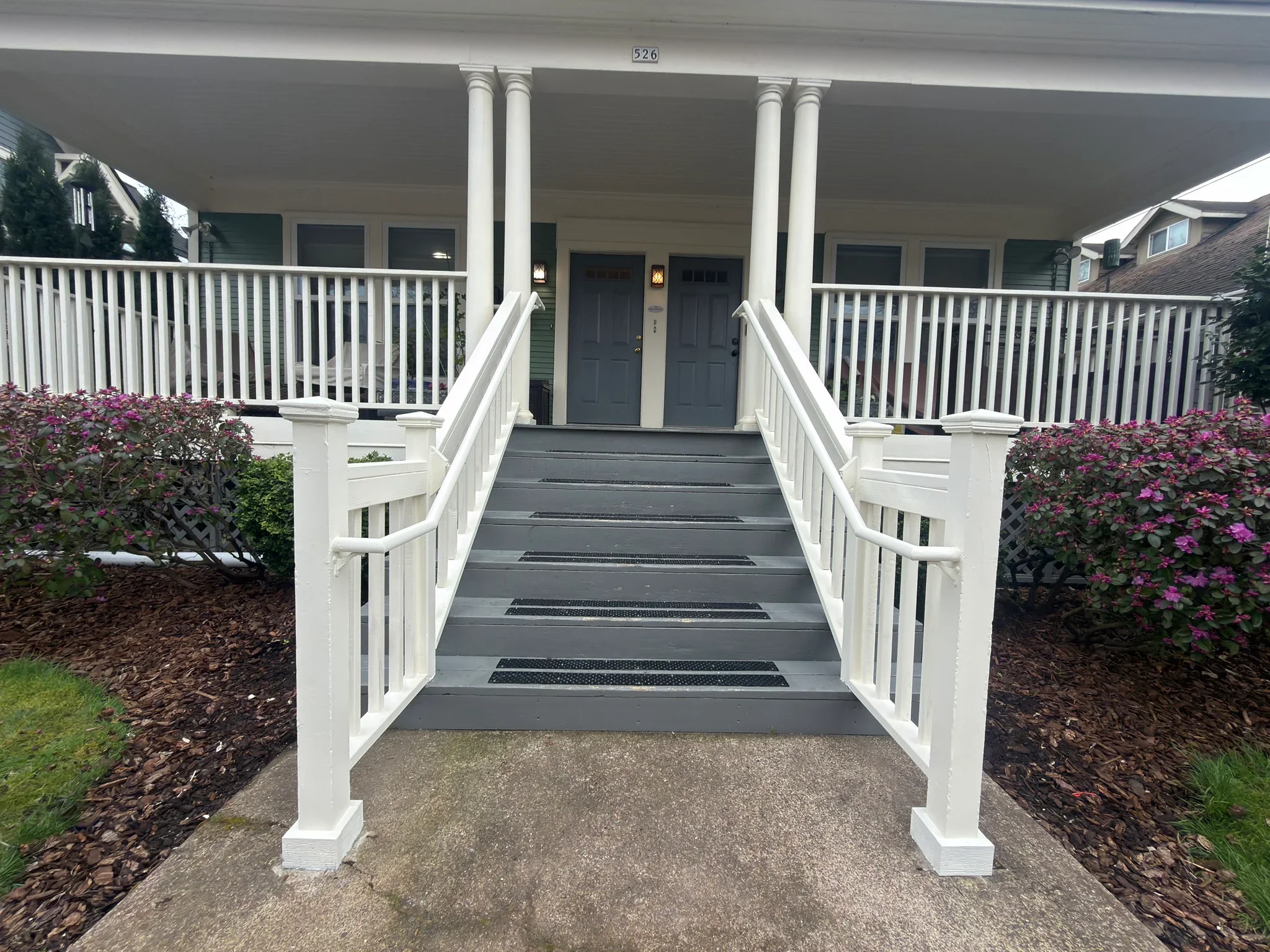 White vinyl railing and composite deck stairs with anti-slip treads leading to covered porch entry