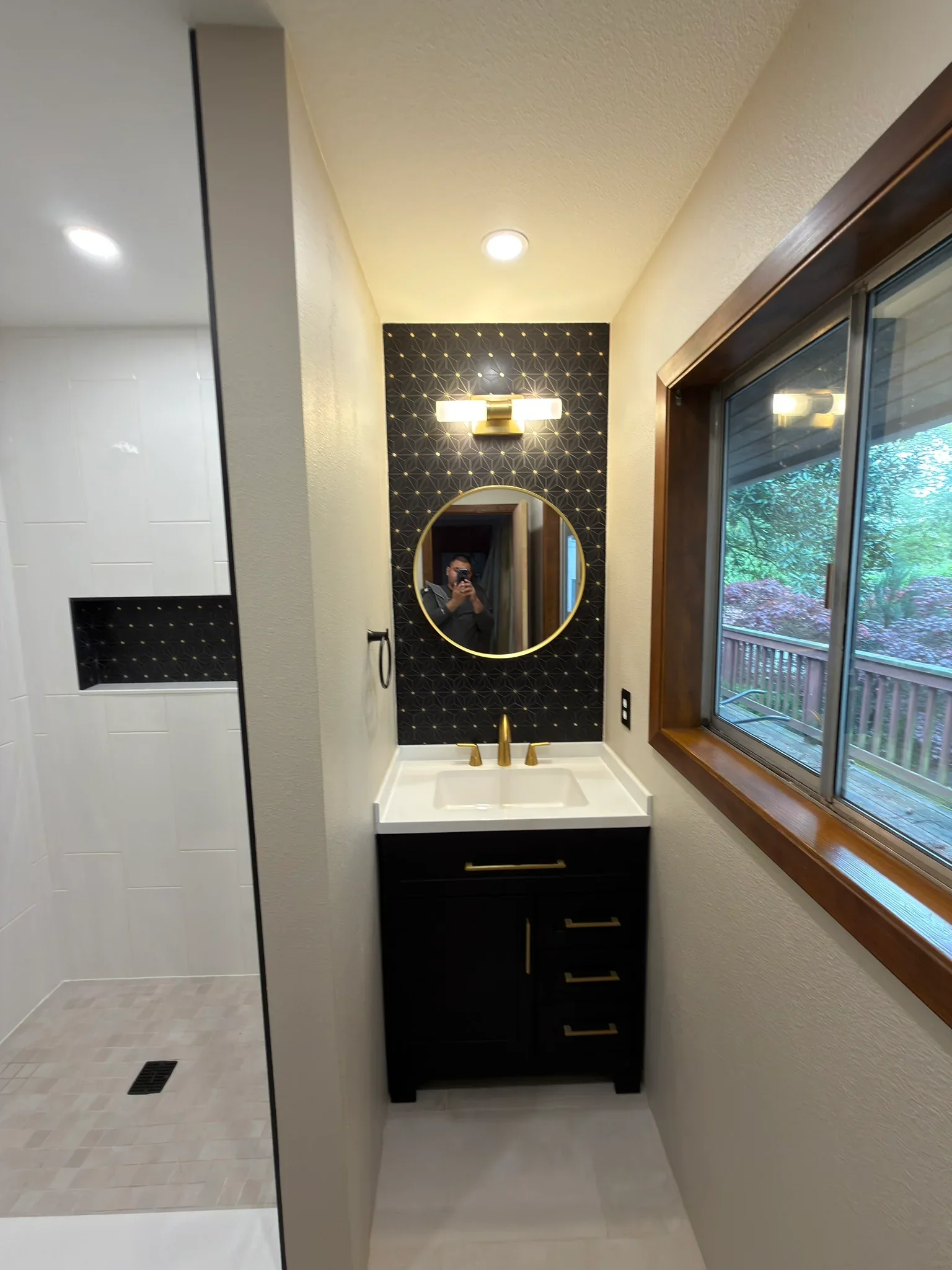 Modern bathroom with black accent wall, circular mirror, black vanity, and white tile shower