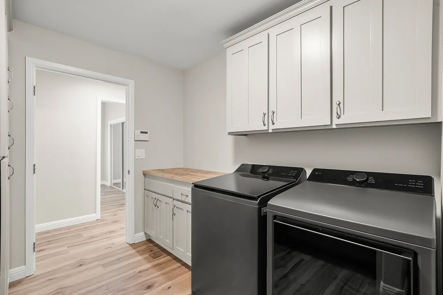Modern laundry room with white cabinets, gray countertops, and black appliances
