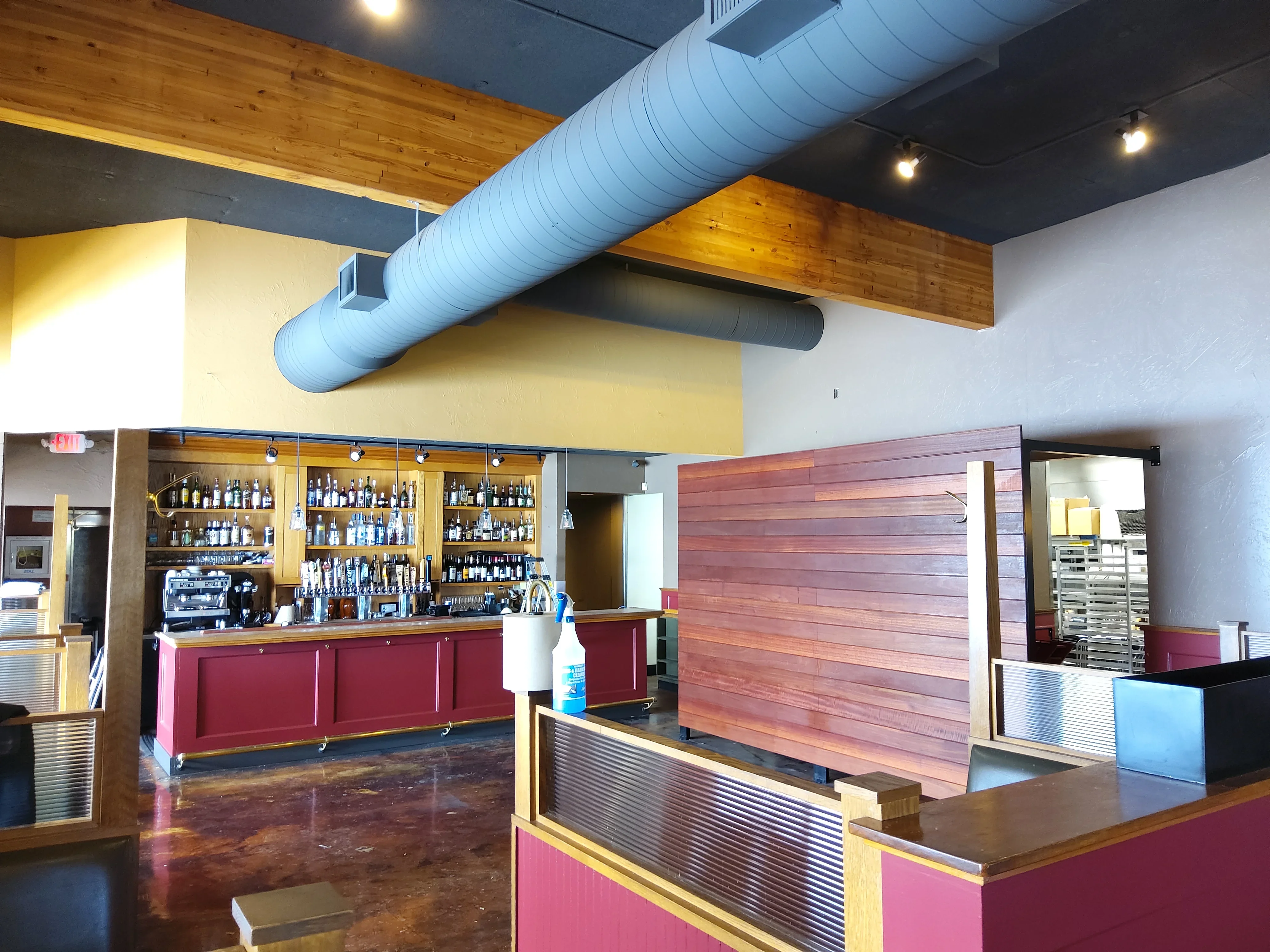 Modern bar interior with burgundy cabinetry, wood accent wall, and exposed ceiling ductwork