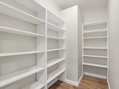 White built-in shelving system in walk-in closet with hardwood flooring