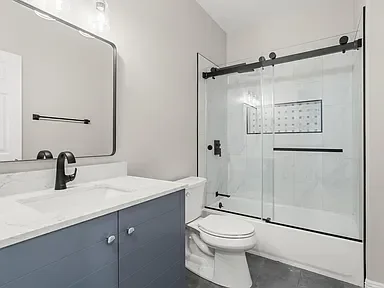 Modern bathroom with blue vanity, quartz countertop, and frameless glass shower