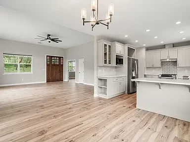 Open kitchen and living room with hardwood floors, white cabinetry, and stainless steel appliances
