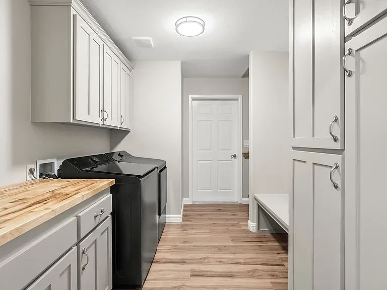 Modern laundry room with gray cabinets, wood countertop, and black washer