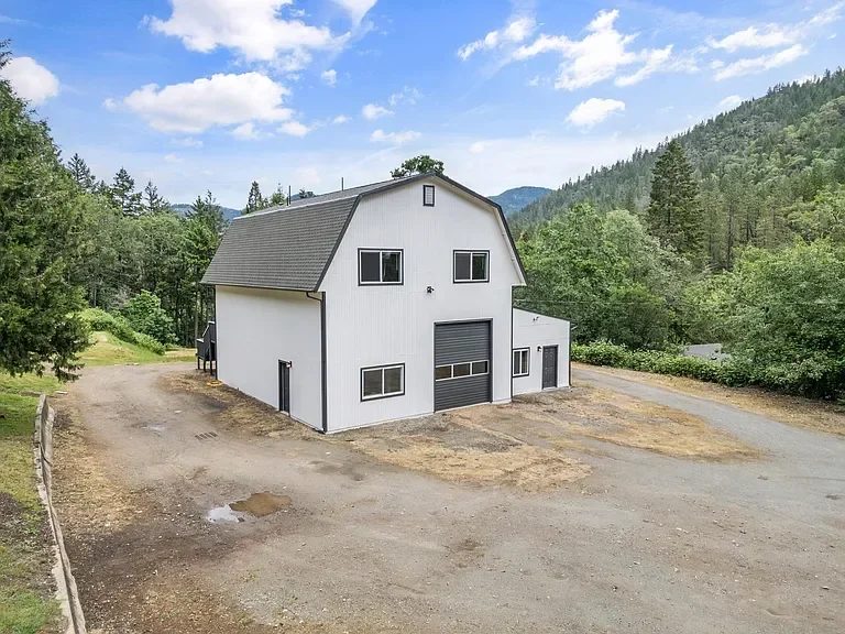White barn-style house with gray metal roof and garage in mountain forest setting