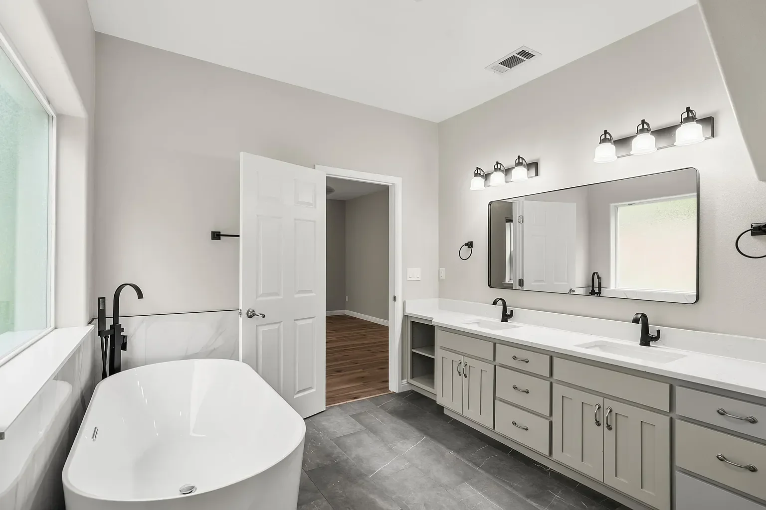 Modern master bathroom with freestanding tub, dual vanity, and gray cabinetry
