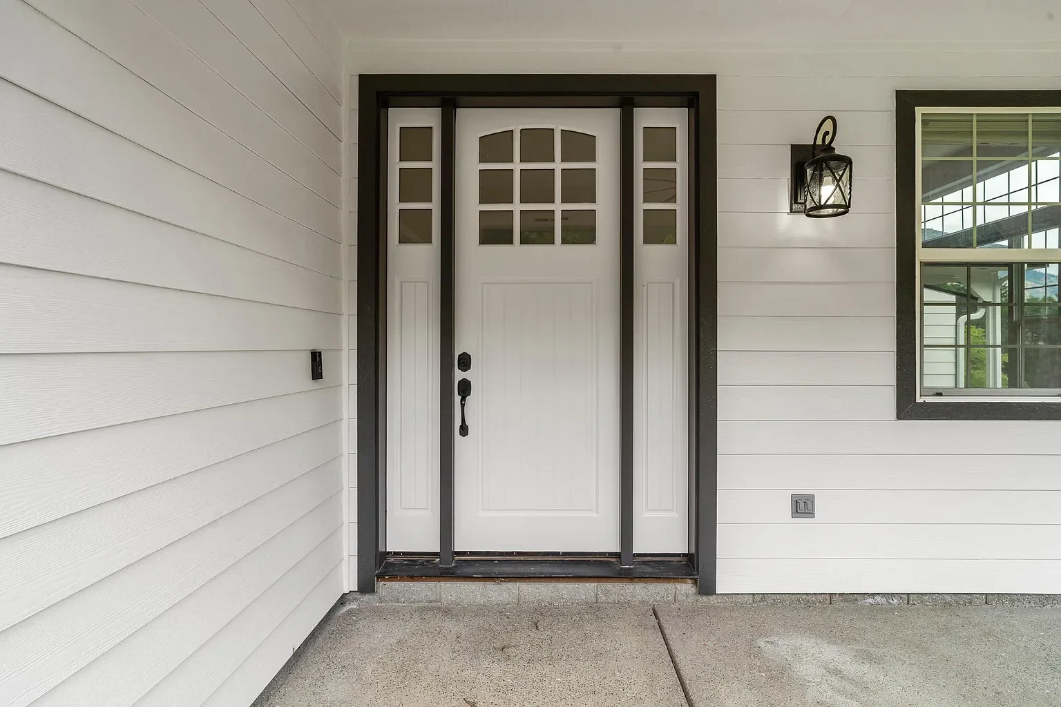 White entry door with sidelights and dark trim on white horizontal siding